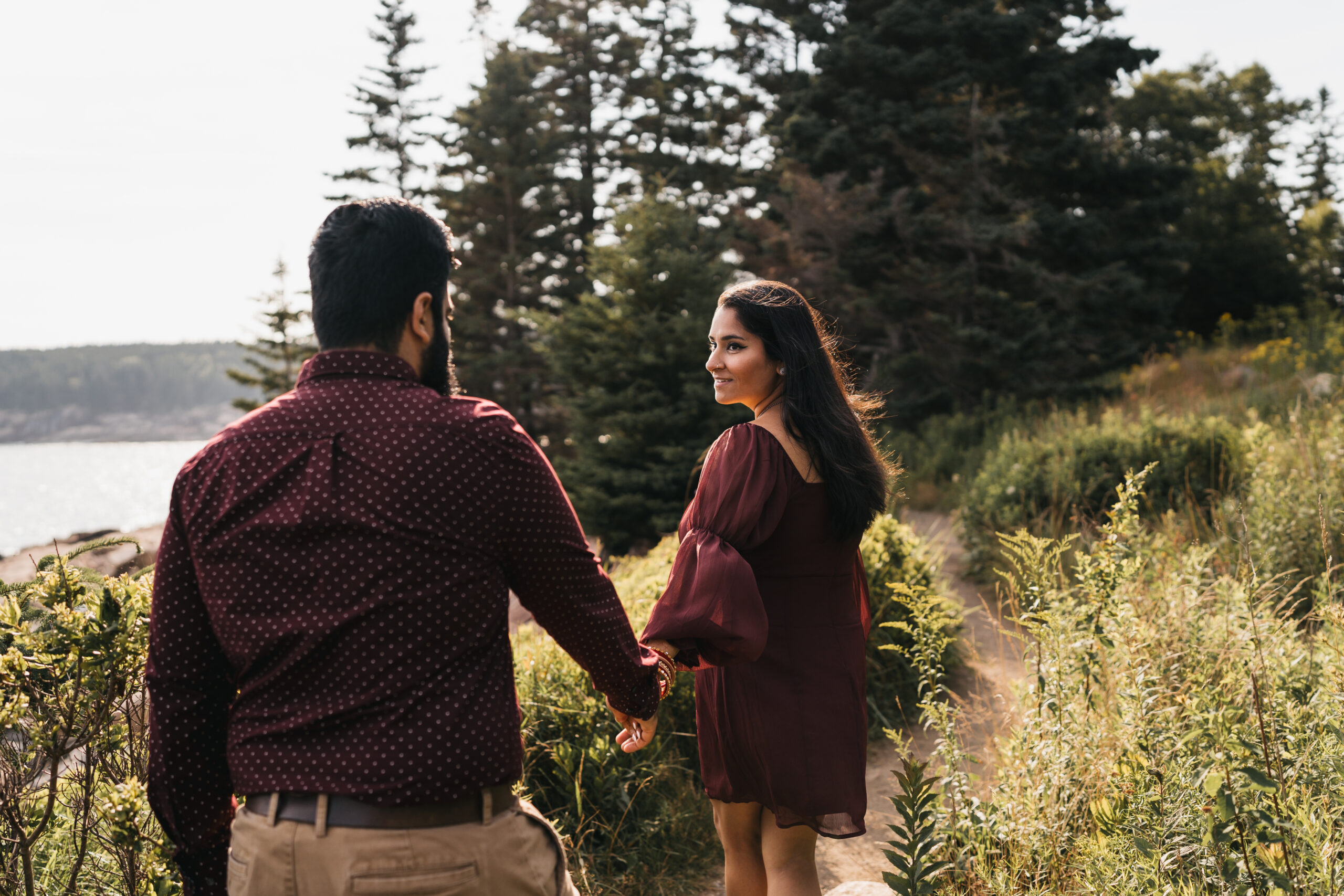 Couple walking hand in hand along the rugged coast of Acadia National Park with ocean views