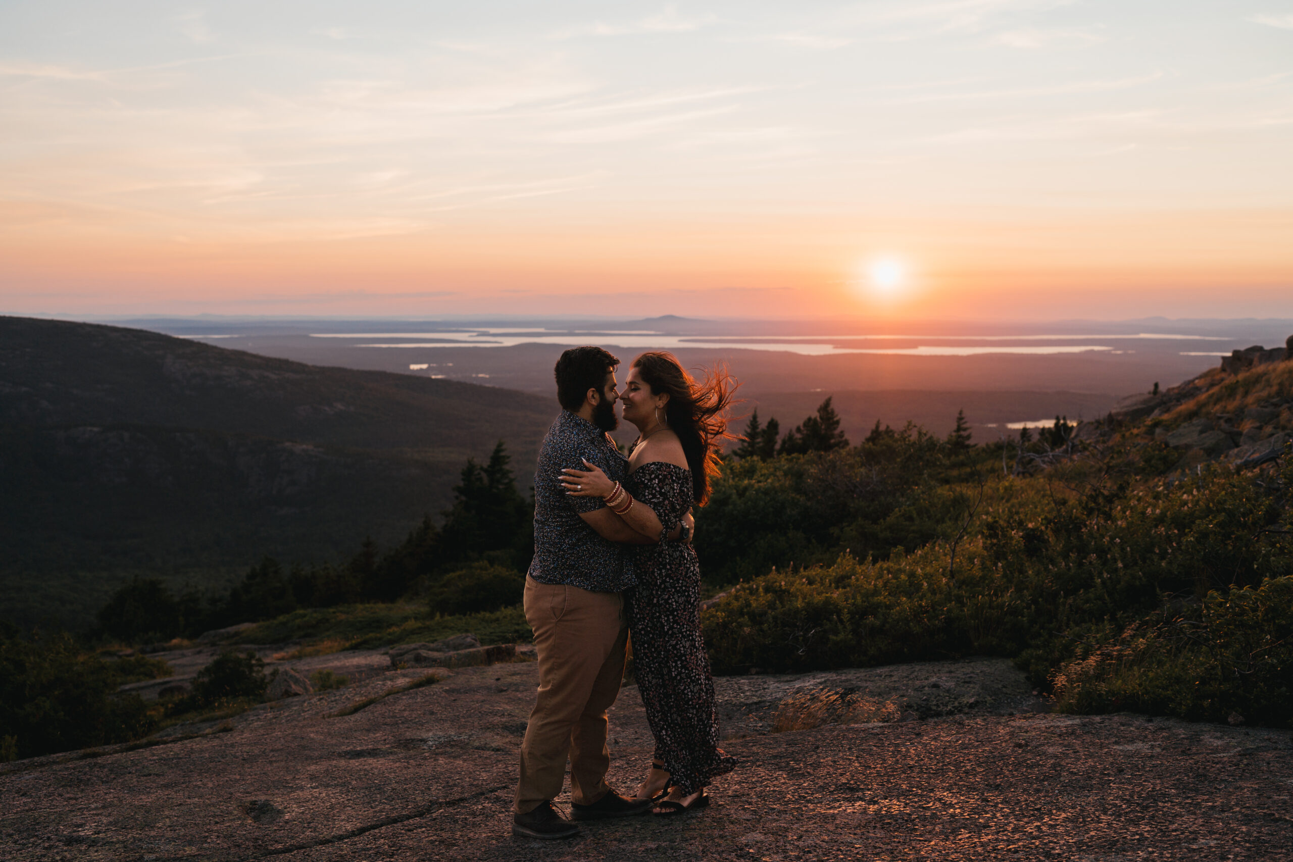 Wind swept portrait of couple on Cadillac Mountain during sunset
