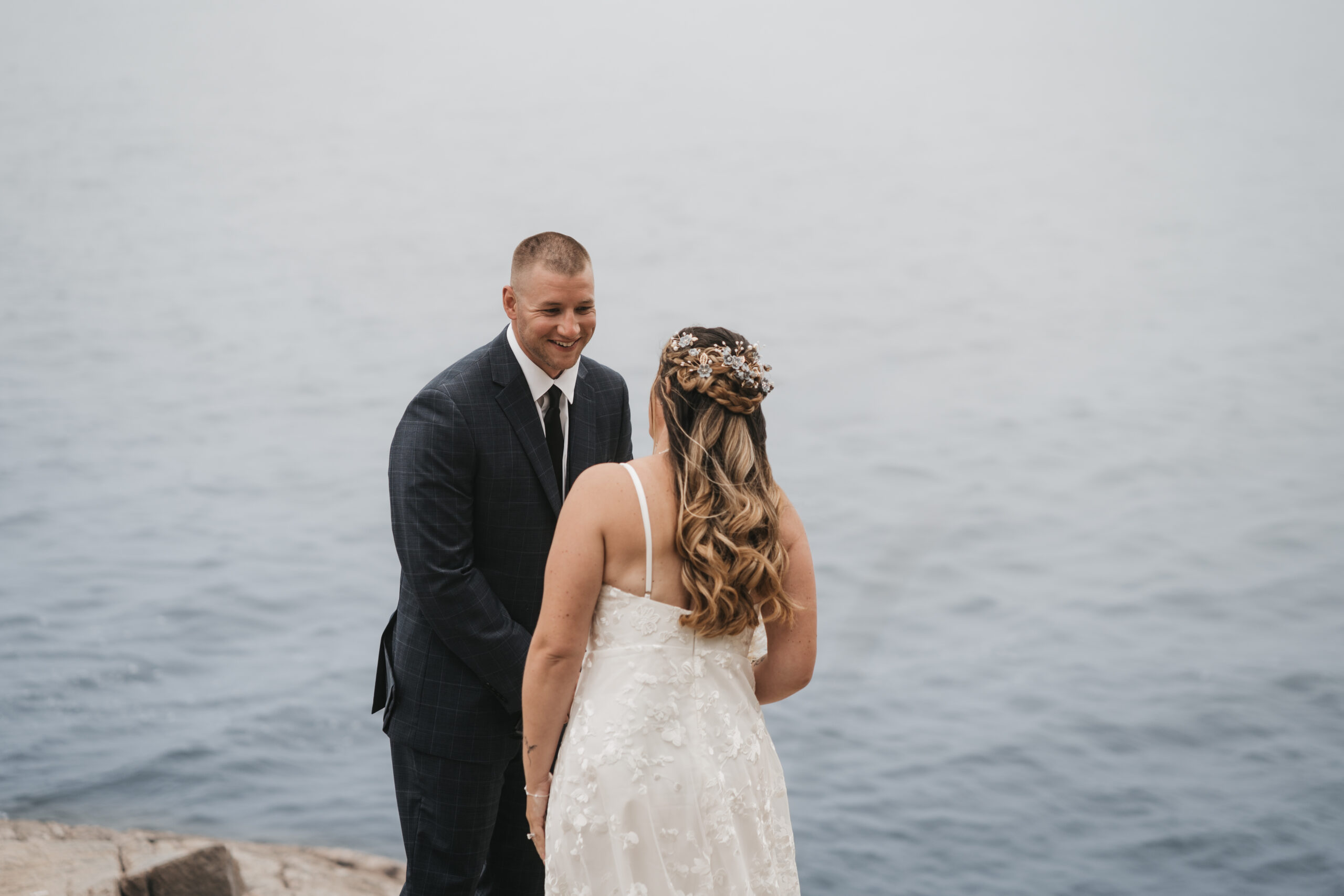 Groom seeing his bride for the first time during their Maine Coastal elopement overlooking Acadia’s rocky coast.