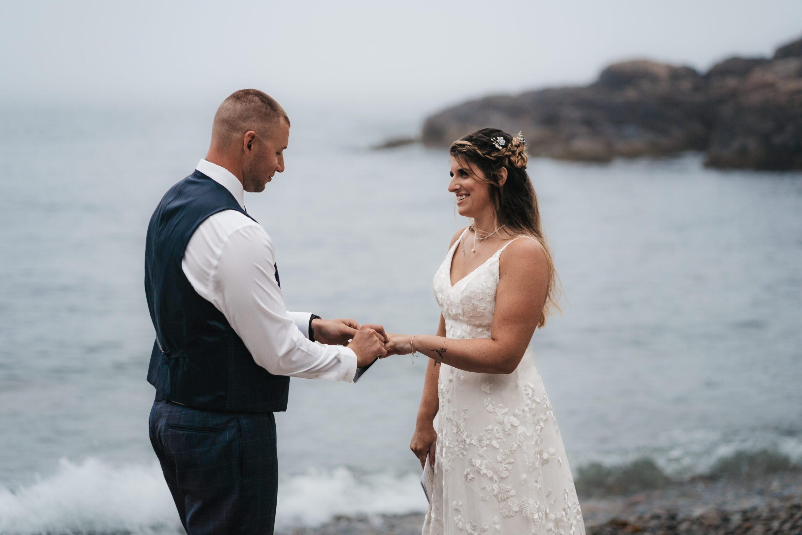 Couple exchanging rings on the pebble shore during their Acadia National Park elopement.