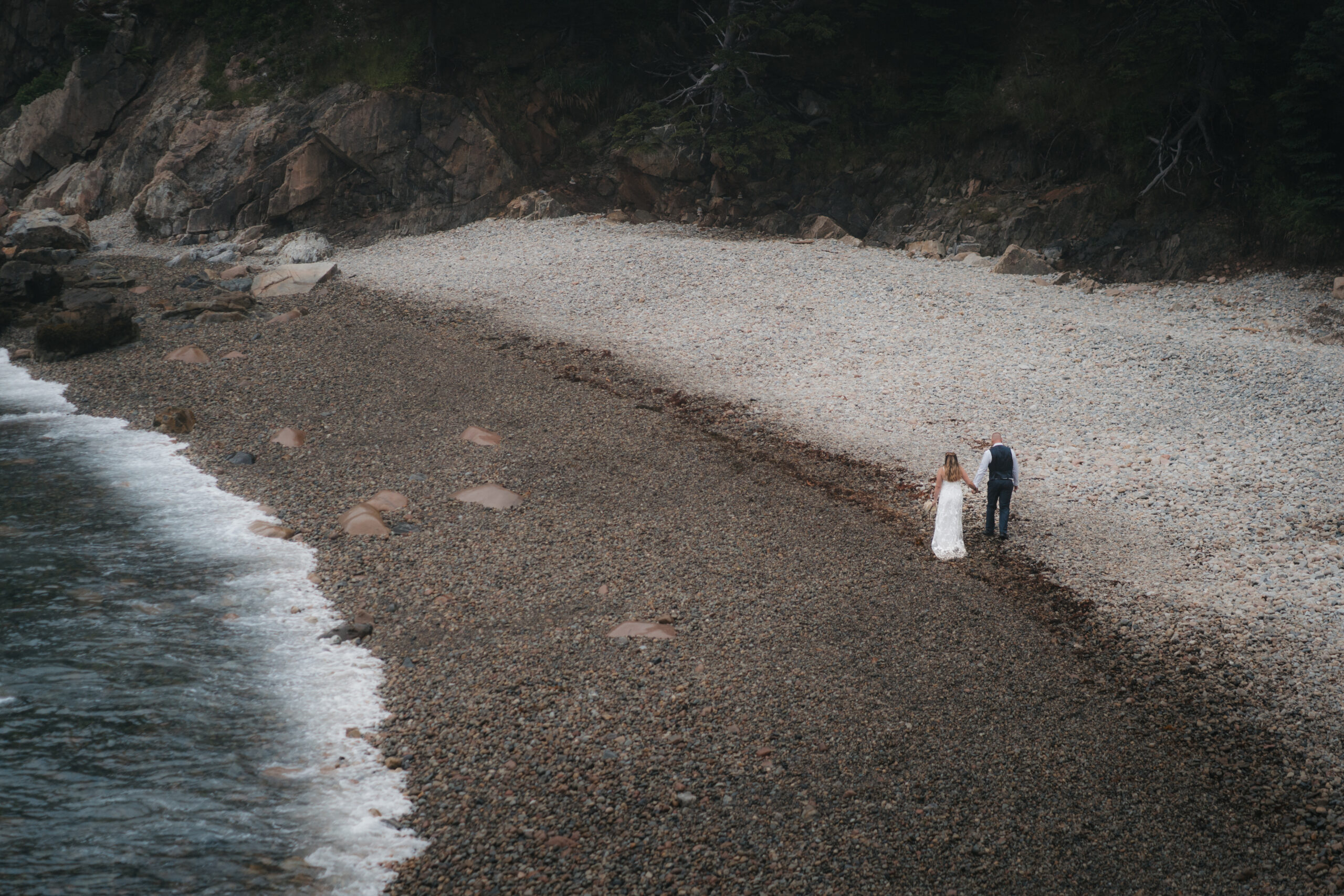 Bride and Groom walking on the pebble shores of Little Hunter's Beach.
