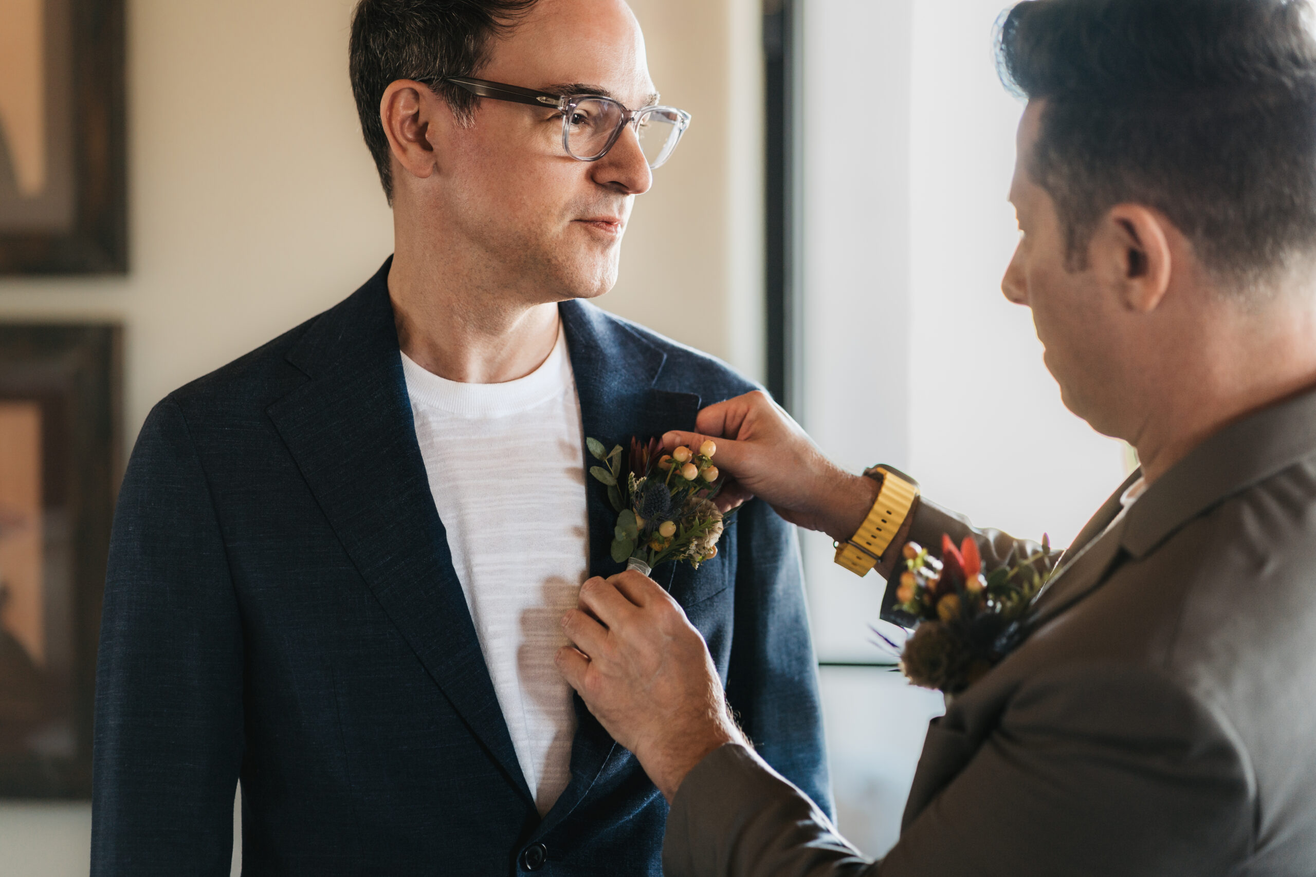 Groom being helped by his best man put on his boutonniere.