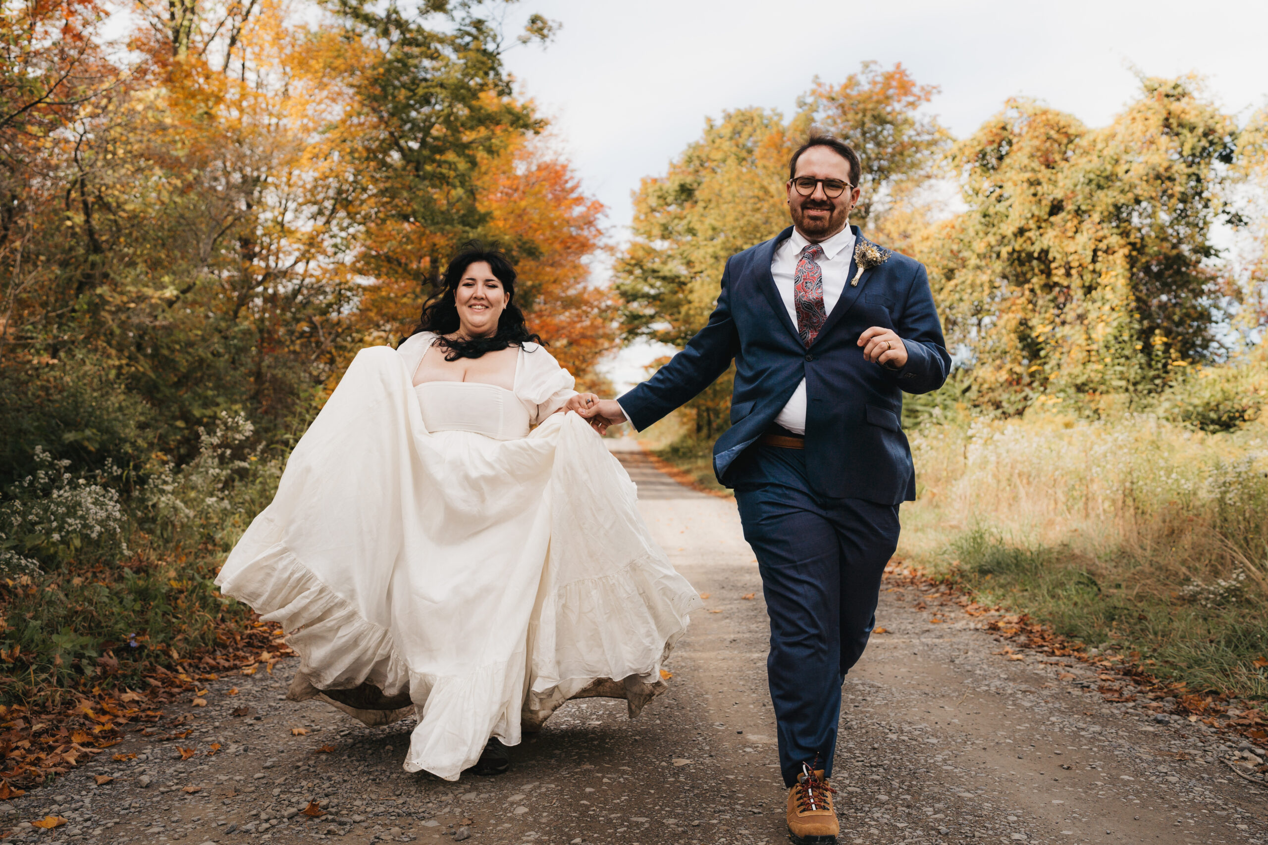 Bride and groom laughing together on scenic fall road during their wedding day.