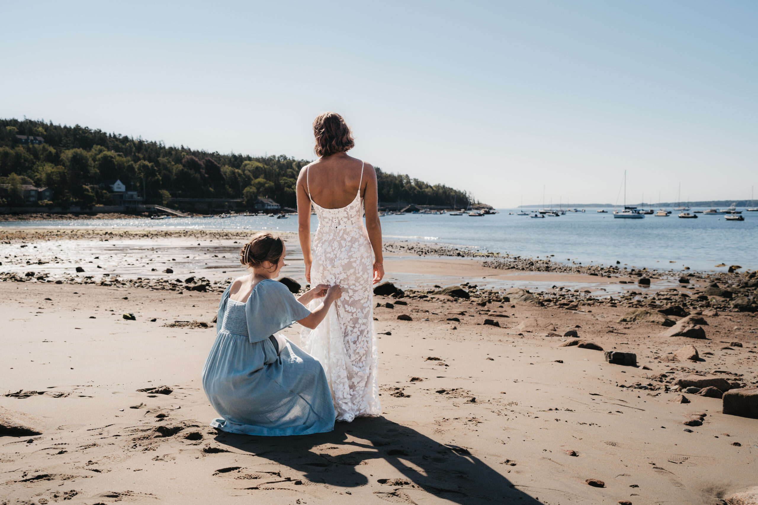 Maid of honor helping the bride bustle her dress at Seal Harbor Beach.