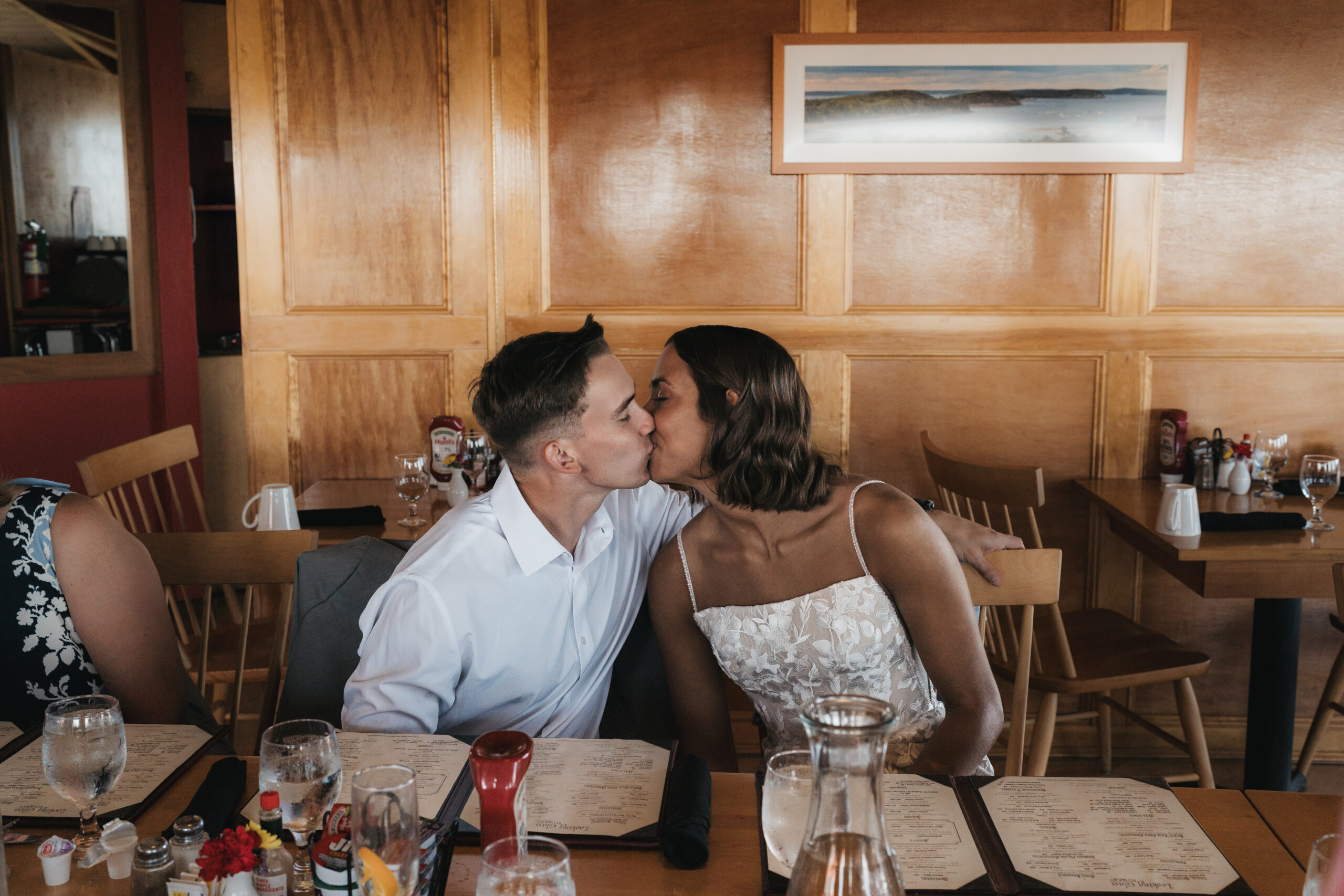 Newlyweds sharing a kiss during their brunch with family in Acadia National Park.